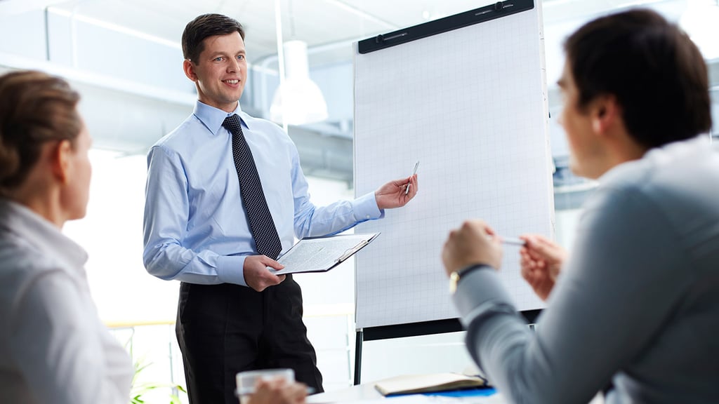 Two people listening to trainer by a flipchart.